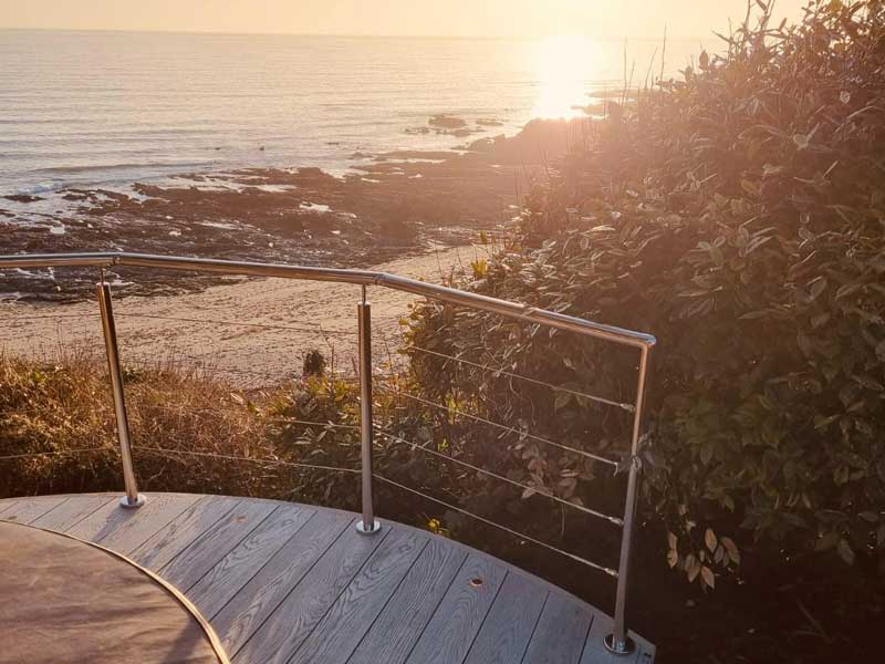 circular deck with glass balustrade overlooking a beautiful cornish beach at sunset