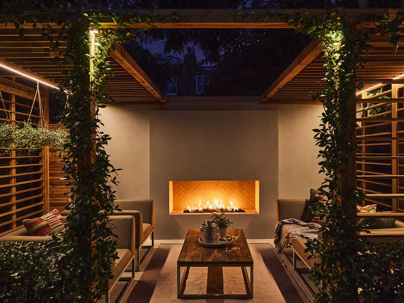 an outdoor fireplace provides a warm glow  in a softly lit outdoor seating area designed by Lilly-Joan Richardson